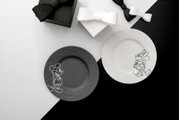 Draufsicht auf zwei dekorative Teller in Schwarz und Weiß mit skizzierten Mickey- und Minnie-Mouse-Motiven, arrangiert auf einem schwarz-weißen Hintergrund mit Geschenkboxen und Schleifen.