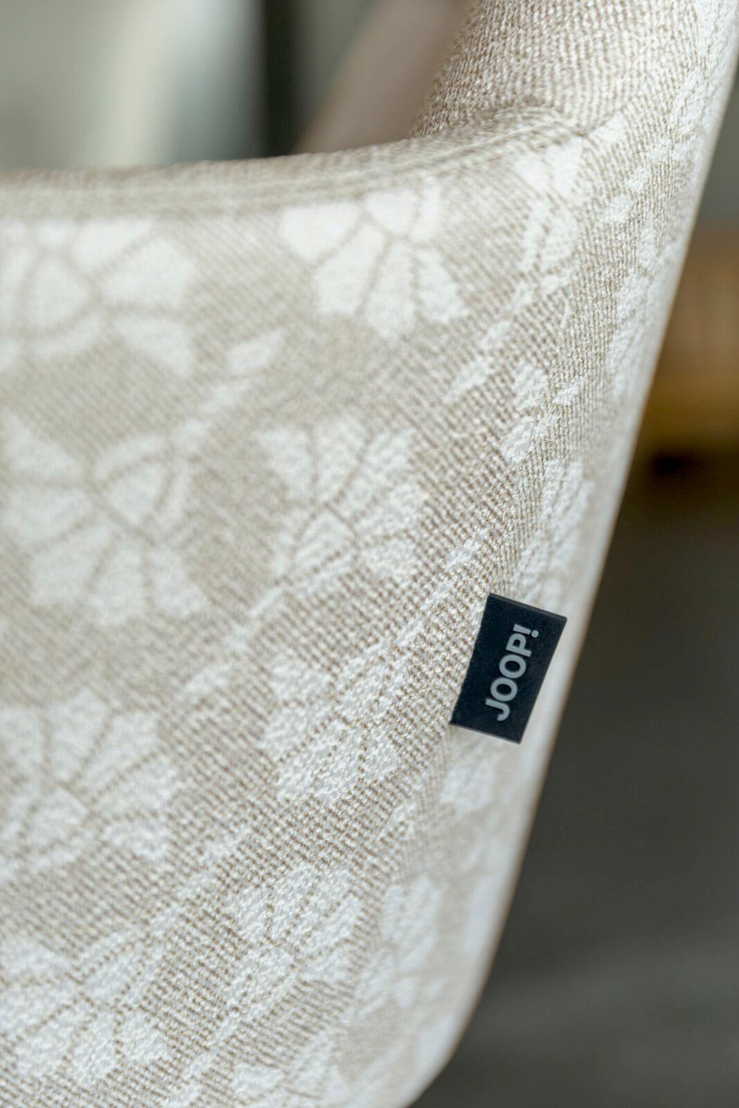 Detailaufnahme aus seitlicher Perspektive: beige-weiß gemustertes Joop!-Textil mit eingewebtem Blumenmuster und sichtbarem Joop!-Label