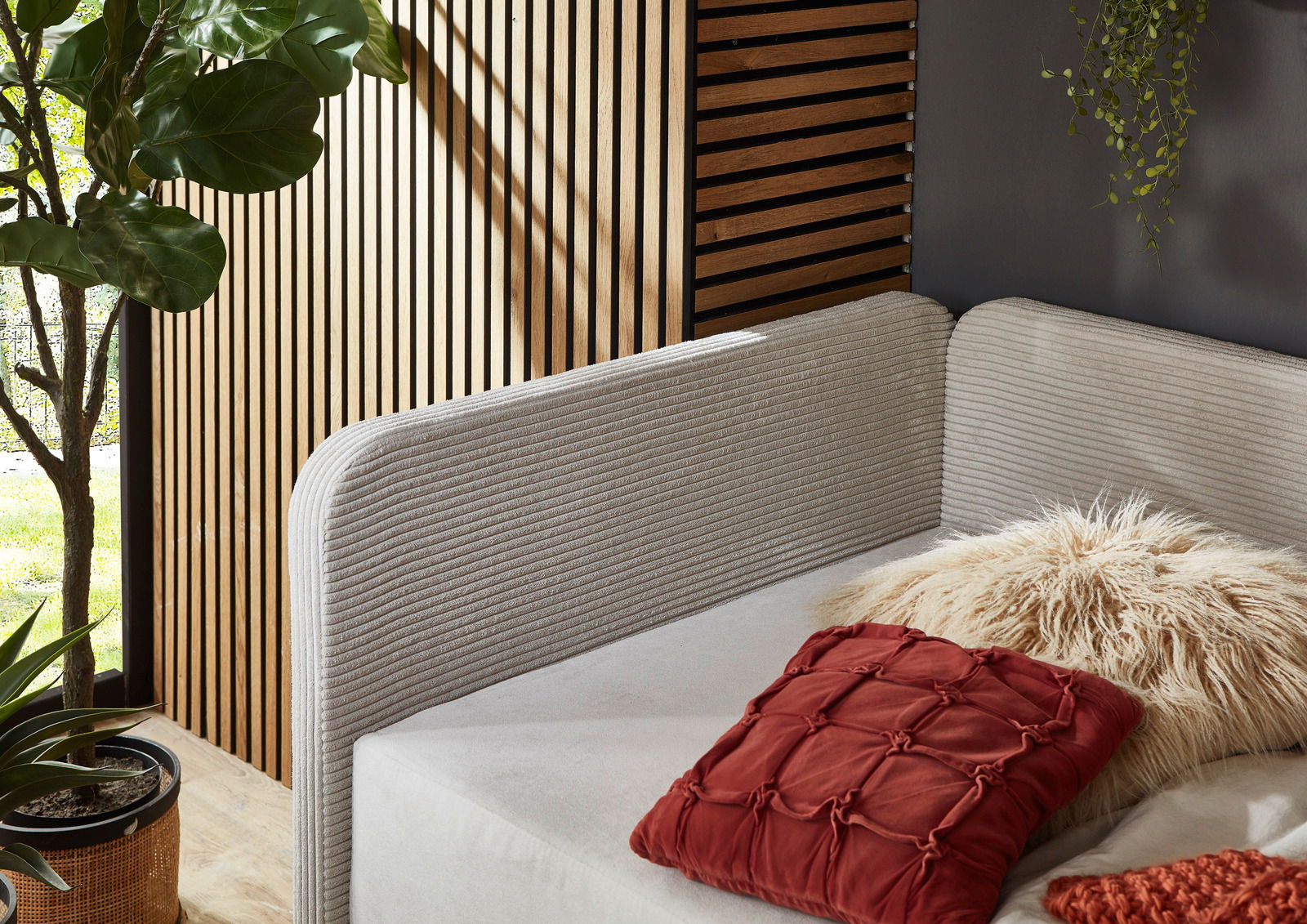 Gemütliches Polsterbett mit weichem, geripptem Kopfteil in einer modernen, natürlichen Umgebung. Perspektive von der Seite.