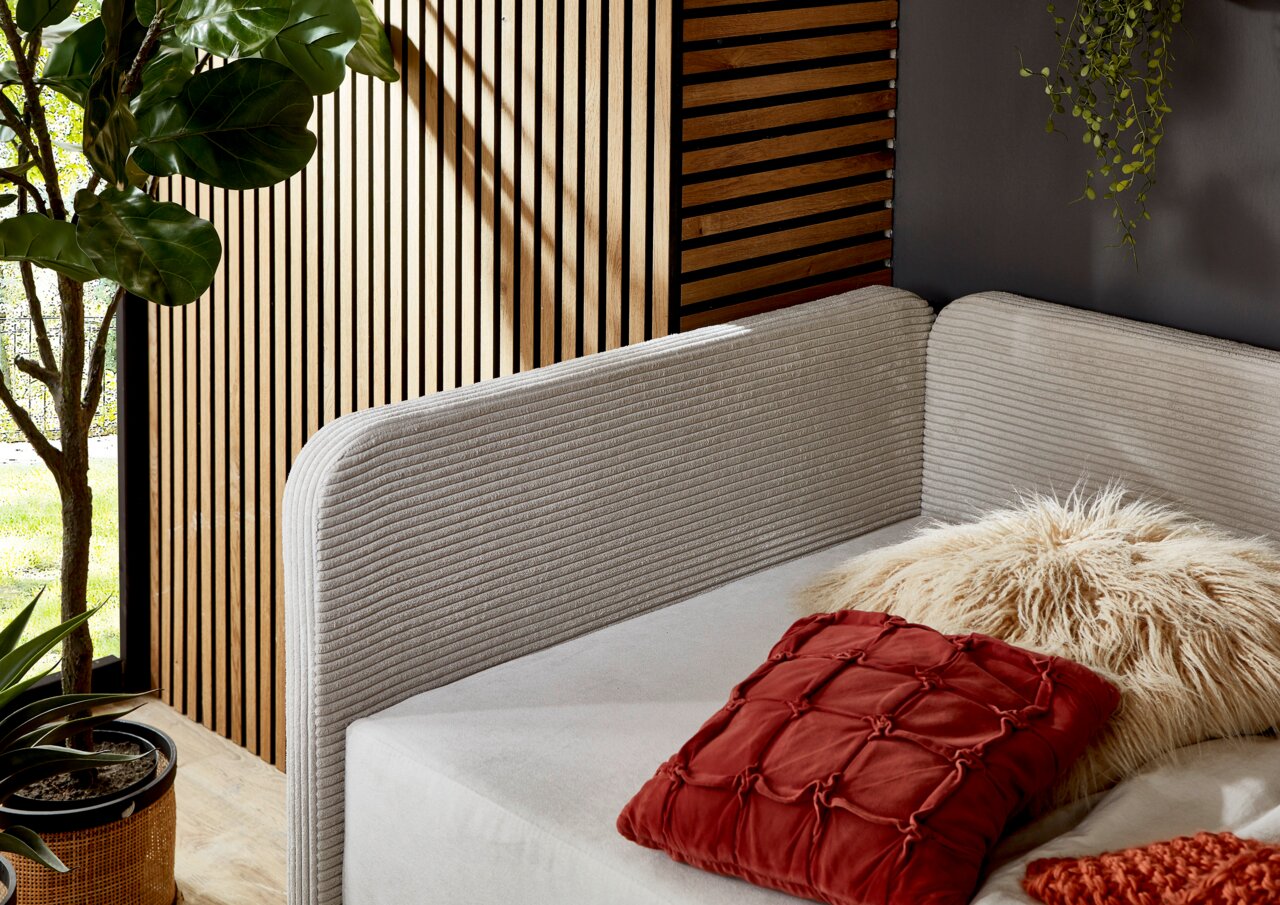 Gemütliches Polsterbett mit weichem, geripptem Kopfteil in einer modernen, natürlichen Umgebung. Perspektive von der Seite.