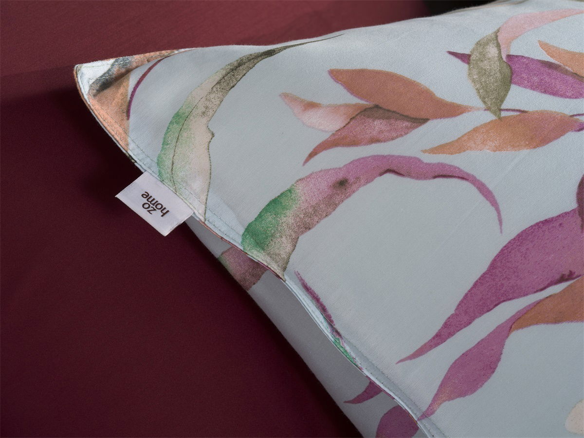 Nahaufnahme einer Bettwäsche mit buntem Blattmuster auf hellem Hintergrund, Perspektive von oben.