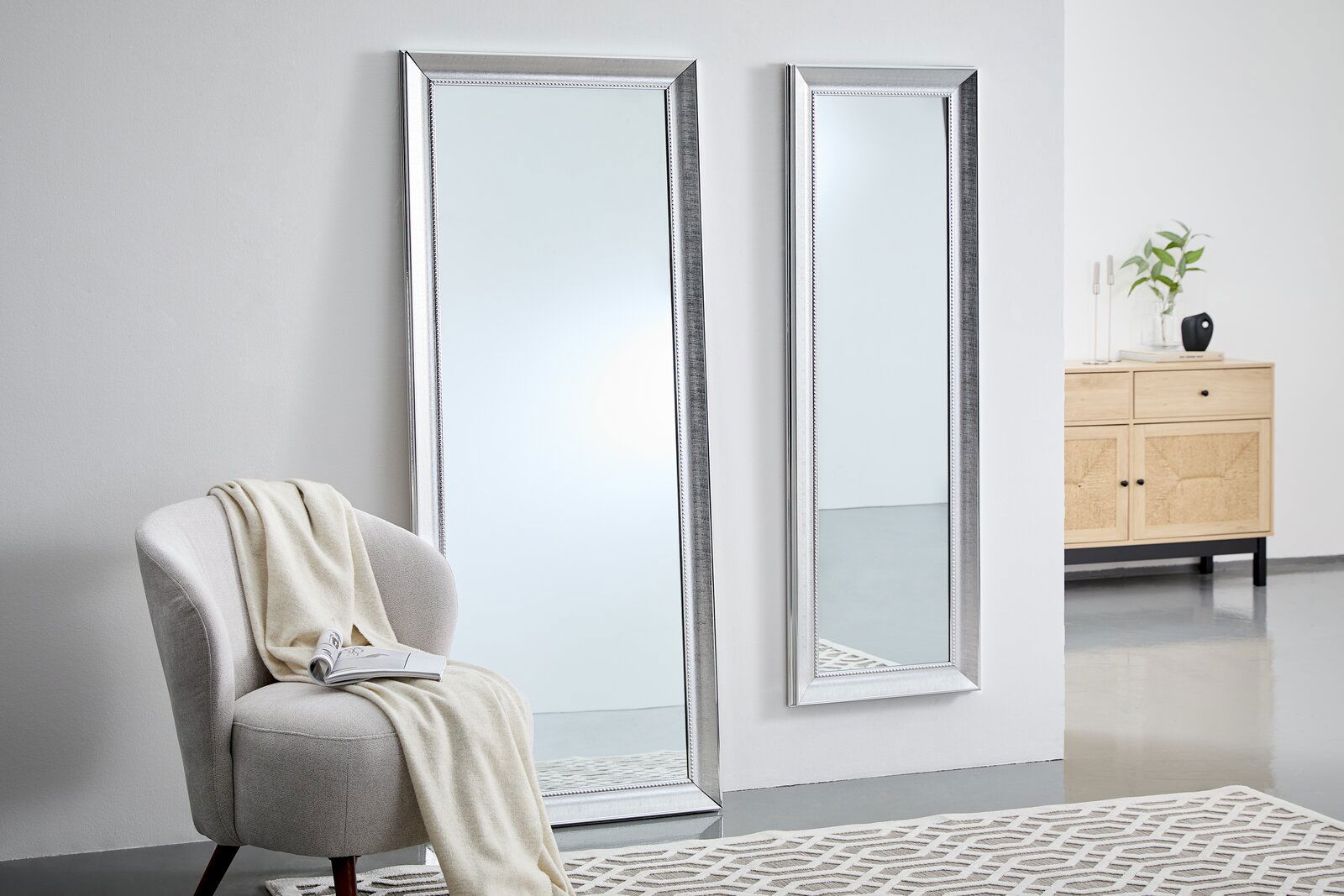XORA Spiegel FELIX Zwei große, rechteckige Spiegel mit silbernem Rahmen, einer steht auf dem Boden, der andere ist an der Wand montiert. Perspektive von schräg vorne.