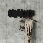 Moderne schwarze Wandgarderobe mit geometrischem Design, frontal an einer Betonwand montiert, mit einem Kleiderbügel und einem Schal dekoriert.