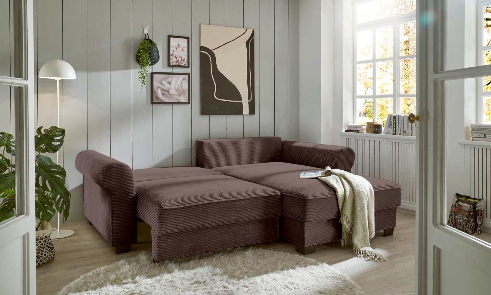 Gemütliche braune Rundecke in einem hellen Wohnzimmer mit großen Fenstern, Pflanzen und moderner Dekoration, seitliche Perspektive.