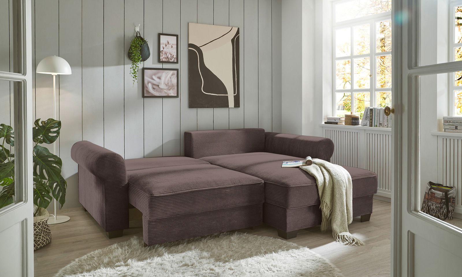 Gemütliche braune Rundecke in einem hellen Wohnzimmer mit großen Fenstern, Pflanzen und moderner Dekoration, seitliche Perspektive.