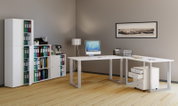 Modernes Büro-Setup mit weißem L-förmigem Schreibtisch und rollbarem Schubladencontainer, Computer und Ablagefächern; perspektivische Ansicht schräg von vorn rechts.