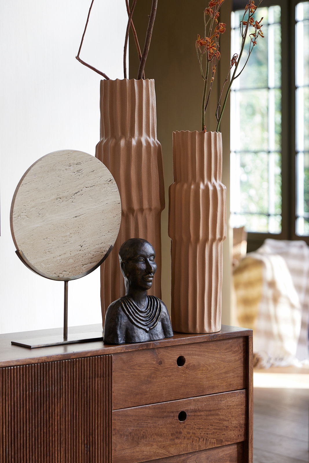 Light&Living Ornament MORENO Zwei hohe, geriffelte Vasen in Erdtönen mit Zweigen und Blumen, daneben eine Büste und ein runder, steinartiger Dekorationsgegenstand auf einem Holzschrank. Perspektive: seitlich.