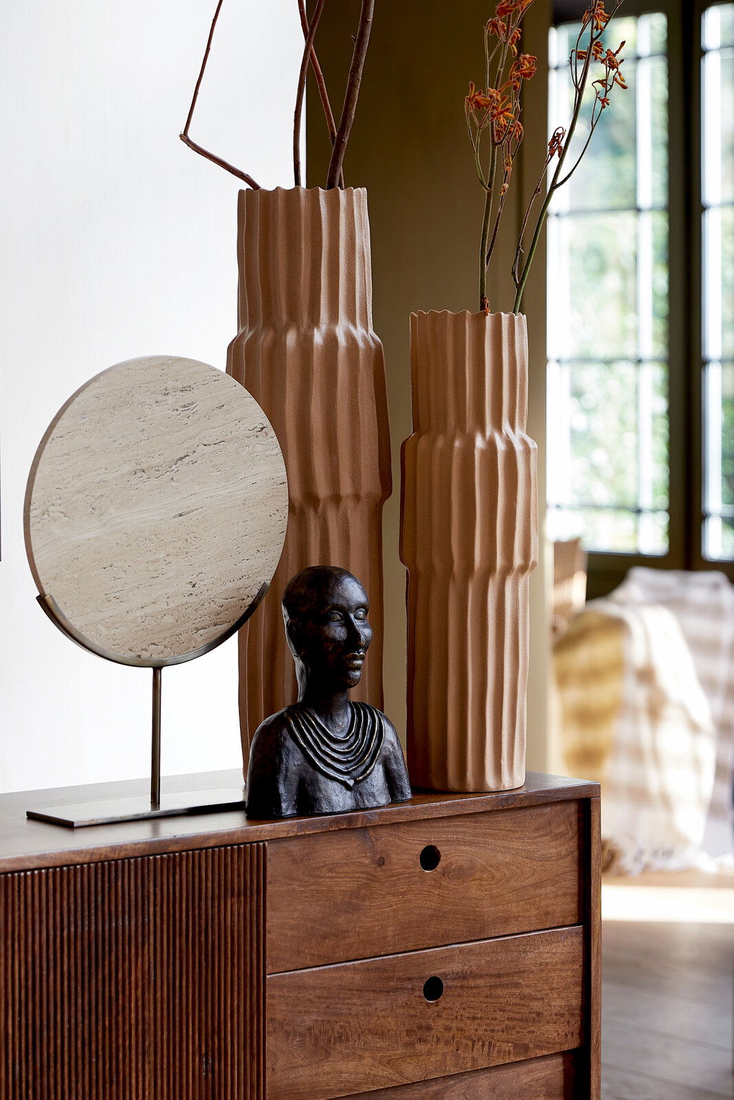 Light&Living Ornament MORENO Zwei hohe, geriffelte Vasen in Erdtönen mit Zweigen und Blumen, daneben eine Büste und ein runder, steinartiger Dekorationsgegenstand auf einem Holzschrank. Perspektive: seitlich.