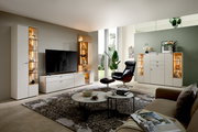 Moderne Wohnzimmeransicht mit eleganter Vitrine in hellem Holz und Glas, links im Bild, mit dekorativer Beleuchtung und stilvollen Accessoires.