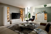 Moderne Wohnzimmeransicht mit eleganter Vitrine in hellem Holz und Glas, links im Bild, mit dekorativer Beleuchtung und stilvollen Accessoires.
