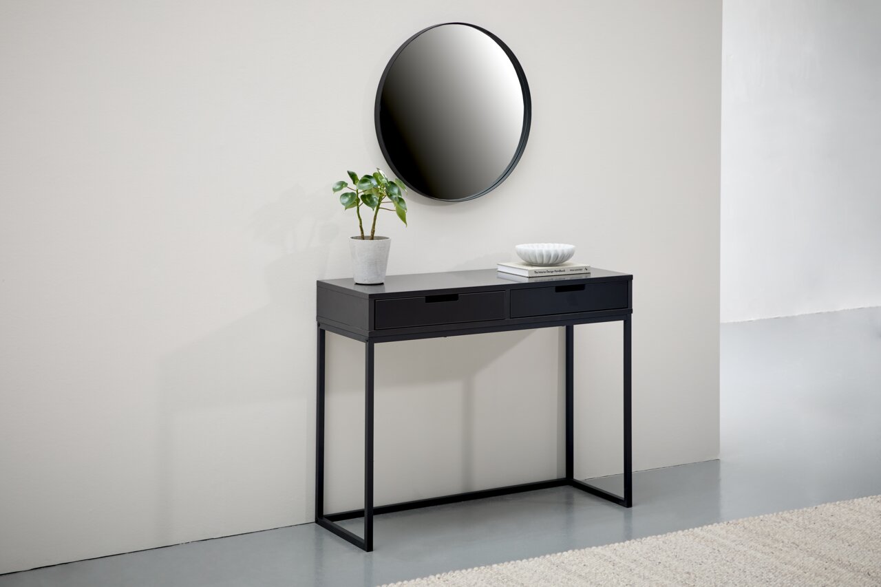 Schwarze Konsole mit zwei Schubladen, dekoriert mit einer Pflanze und einer Schale, vor einem runden Spiegel an der Wand. Frontalansicht.