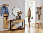 Heller Flur mit Garderobenmöbeln aus Massivholz und schwarzem Metall: Wandgarderobe mit Jacke, Konsolentisch mit rundem Spiegel und Deko sowie freistehender Garderobenständer am Fenster, frontal aus leicht schräger Perspektive fotografiert.