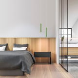Zwei grüne Akku-Pendelleuchten hängen von der Decke über einem modernen Schlafzimmer mit Holzverkleidung und grauer Bettwäsche. Perspektive: seitlich.