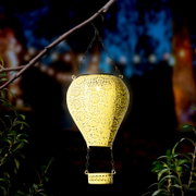 Metallener Solarballon in Form eines Heißluftballons, aufgehängt an einem Ast, leuchtet in der Dämmerung. Perspektive von vorne.