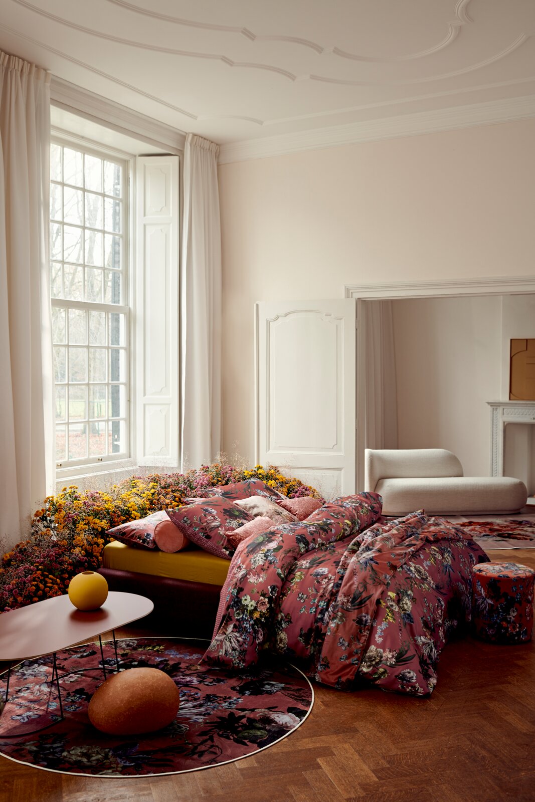 Aus leicht erhöhter Frontalperspektive präsentiertes Bett mit üppiger, dunkelrosa geblümter Bettwäsche und dekorativen Kissen in einem eleganten, lichtdurchfluteten Schlafzimmer.