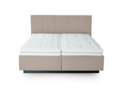 Vooraanzicht van een gestoffeerd bed met twee witte matrassen en een gestoffeerd hoofdeinde in beige.
