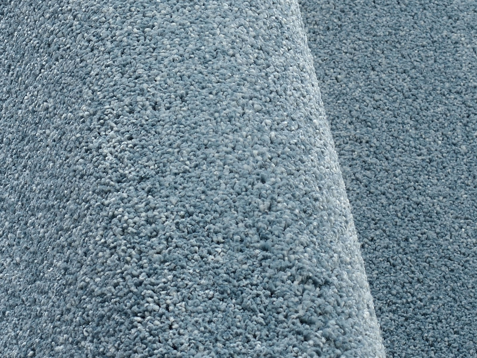 Nahaufnahme eines blauen Uni-Teppichs mit weicher, flauschiger Textur, seitliche Perspektive.