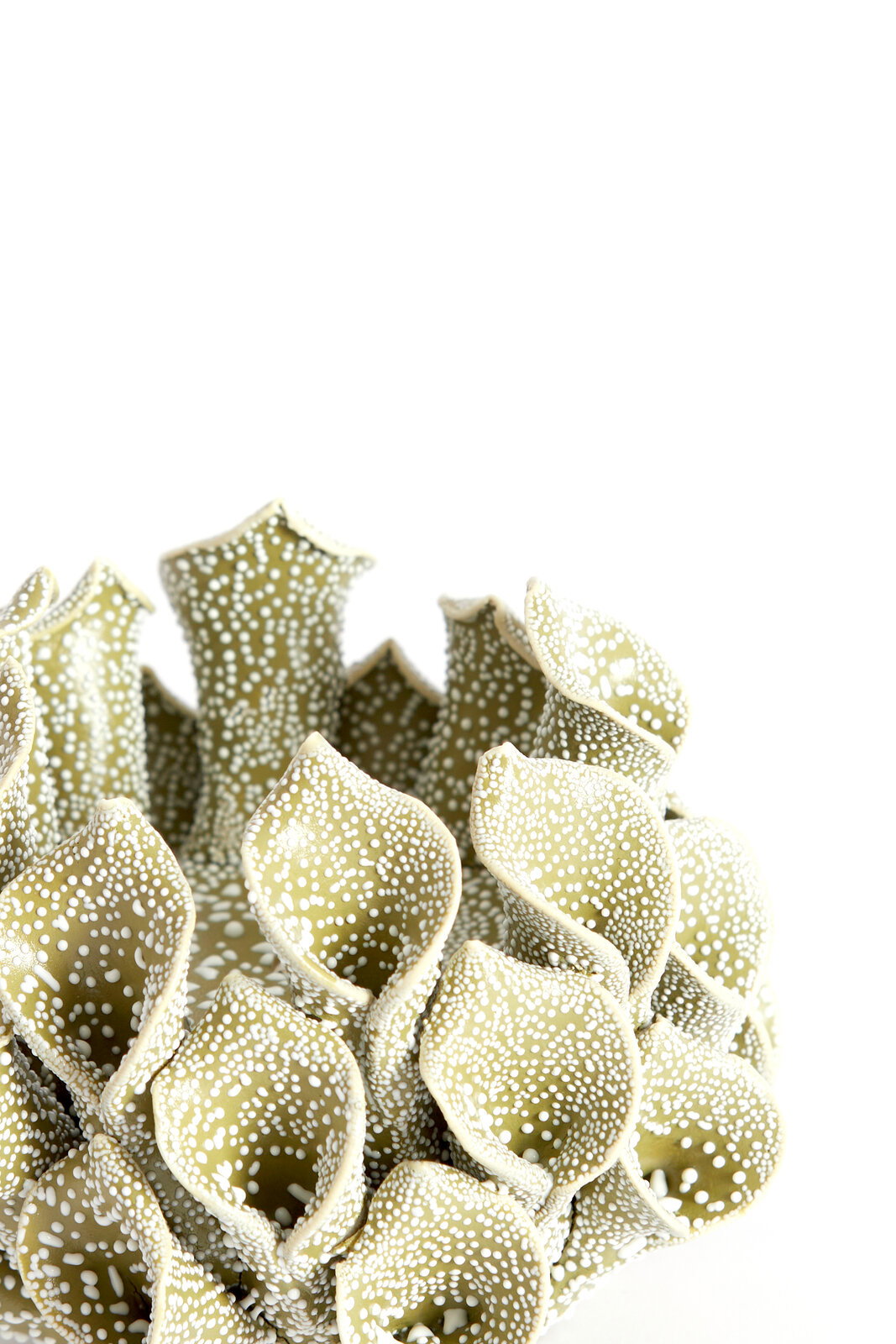 Nahaufnahme eines dekorativen Teelichthalters in organischer Form mit grünlichen, punktierten Strukturen, die an Korallen erinnern.