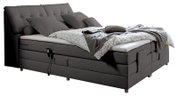 Graues Boxspringbett mit verstellbarem Kopfteil, mehreren Kissen und einer gemusterten Bettdecke, seitliche Perspektive