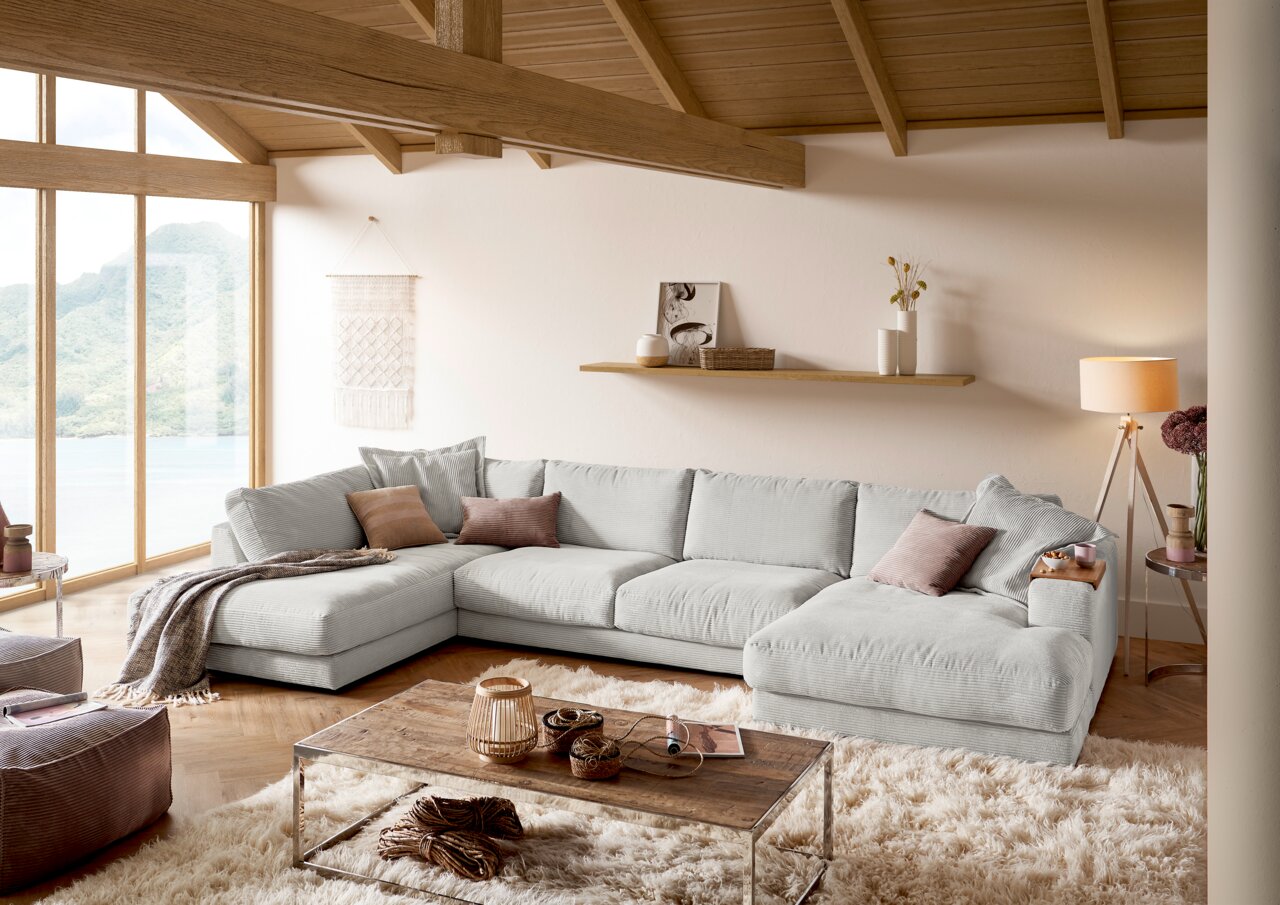 Lounge Handmade Wohnlandschaft LH-SAMBIA Gemütliche Rundecke in einem modernen Wohnzimmer mit großen Fenstern und Holzbalkendecke, aus der Perspektive von vorne links betrachtet.