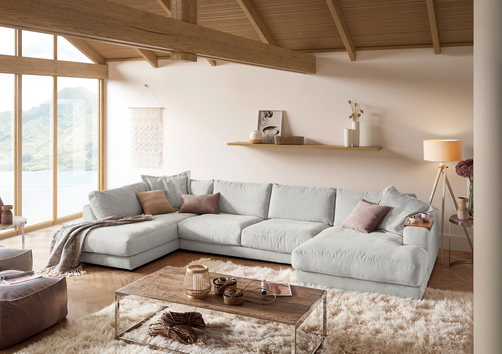 Lounge Handmade Wohnlandschaft LH-SAMBIA Gemütliche Rundecke in einem modernen Wohnzimmer mit großen Fenstern und Holzbalkendecke, aus der Perspektive von vorne links betrachtet.