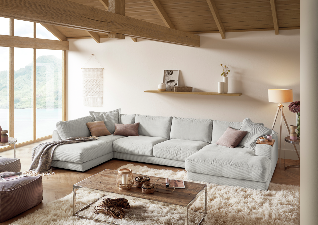 Gemütliche Rundecke in einem modernen Wohnzimmer mit großen Fenstern und Holzbalkendecke, aus der Perspektive von vorne links betrachtet.