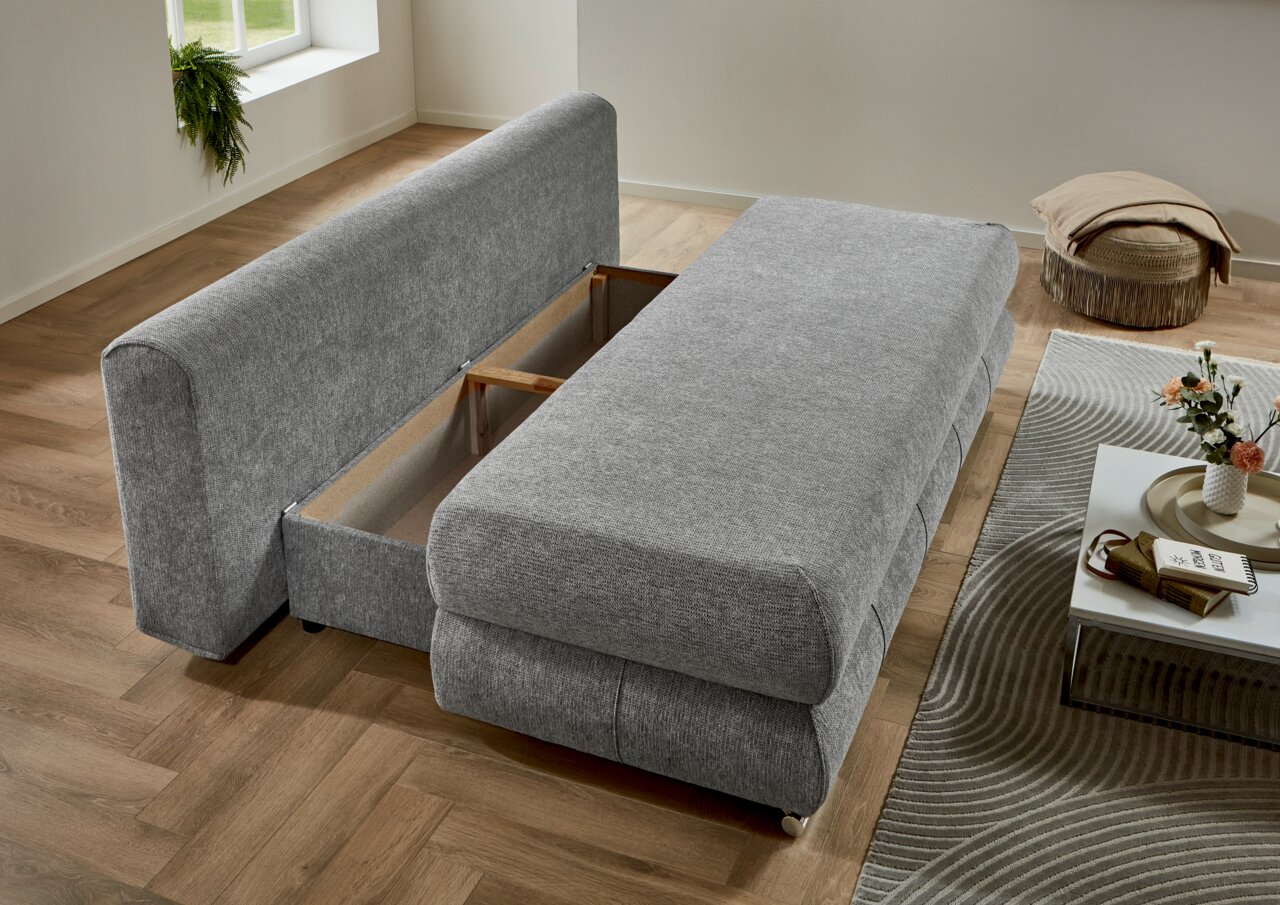 Graues Funktionssofa mit ausgeklapptem Bettkasten, seitliche Perspektive im Wohnzimmer.