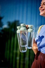 Eine Person hält mehrere Trinkflaschen in der Farbe Nordic Sage in der Hand, im Freien bei sonnigem Wetter.