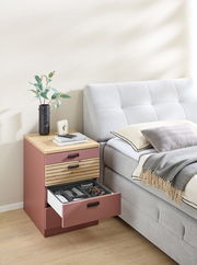 Rollcontainer in einem modernen Schlafzimmer, seitliche Perspektive. Der Container hat eine Holzoberfläche und drei Schubladen, von denen eine geöffnet ist und verschiedene Gegenstände zeigt.