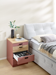 Rollcontainer in einem modernen Schlafzimmer, seitliche Perspektive. Der Container hat eine Holzoberfläche und drei Schubladen, von denen eine geöffnet ist und verschiedene Gegenstände zeigt.