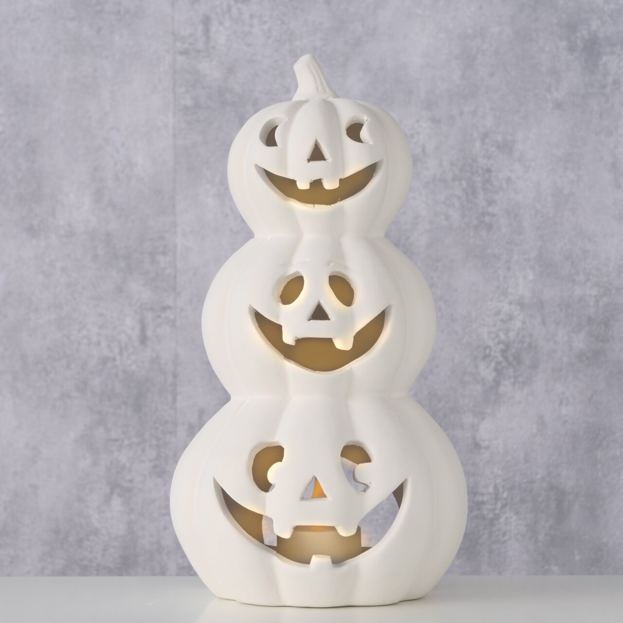 Boltze Teelichthalter Kürbis CURBANA 25cm Weißer Teelichthalter in Form von drei gestapelten Kürbissen mit geschnitzten Gesichtern, frontal betrachtet.
