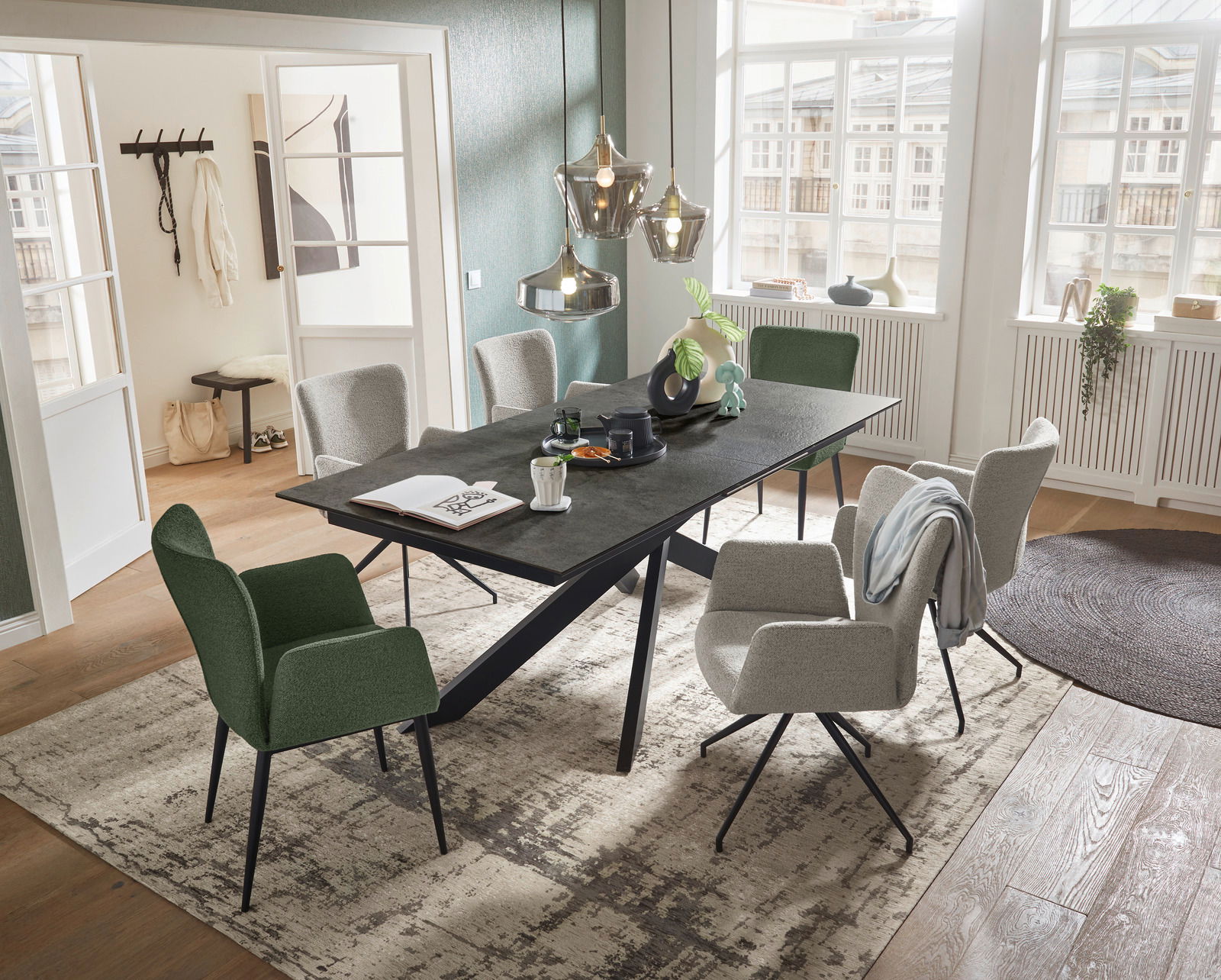 Moderner Esstisch mit schwarzer Tischplatte und schrägen Beinen, umgeben von stilvollen Stühlen in einem hellen, eleganten Raum mit großen Fenstern. Perspektive von oben.