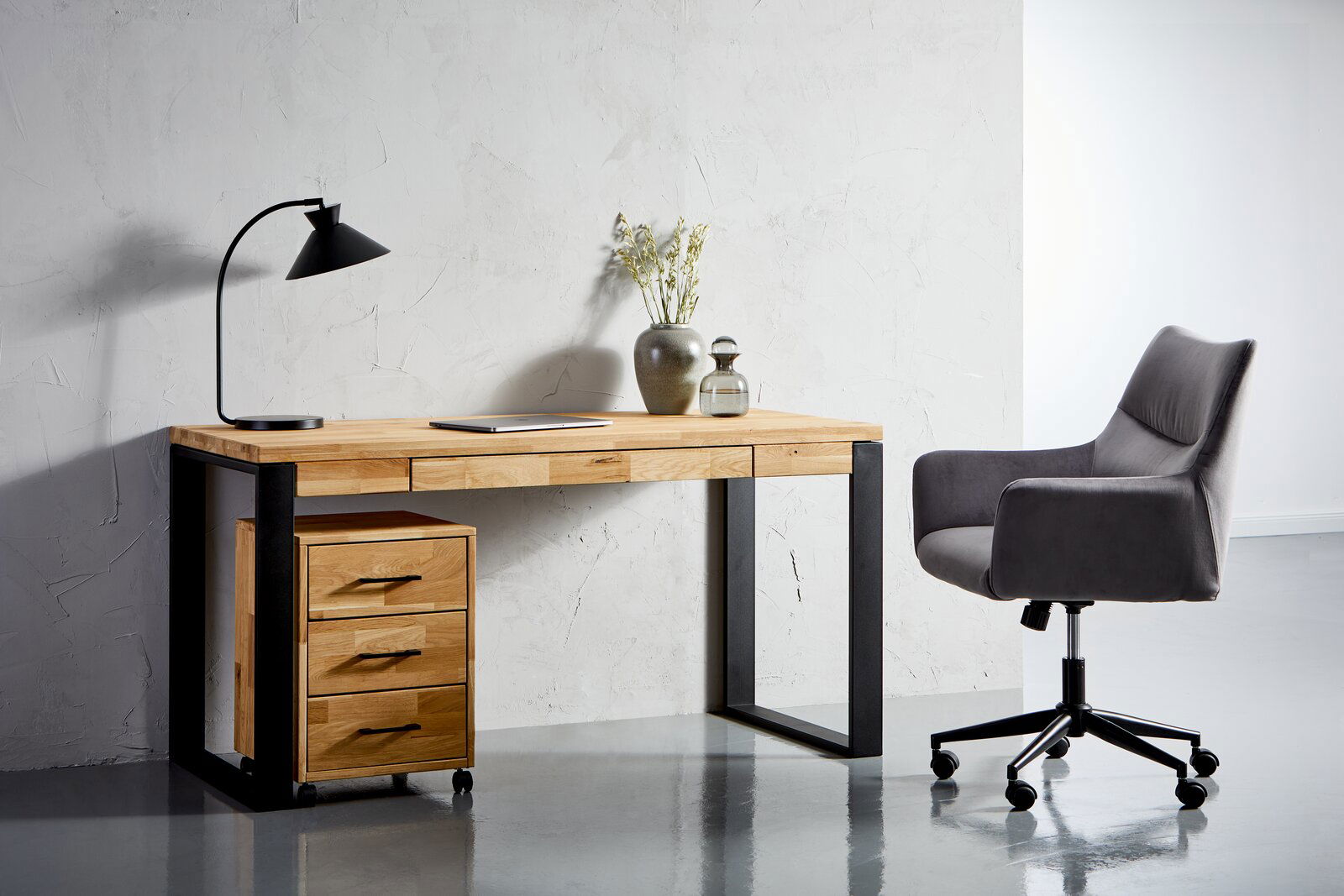 Moderner Schreibtisch aus Holz mit schwarzem Metallgestell, linksseitig mit drei Schubladen, dekoriert mit einer Tischlampe und Vasen, seitliche Perspektive.