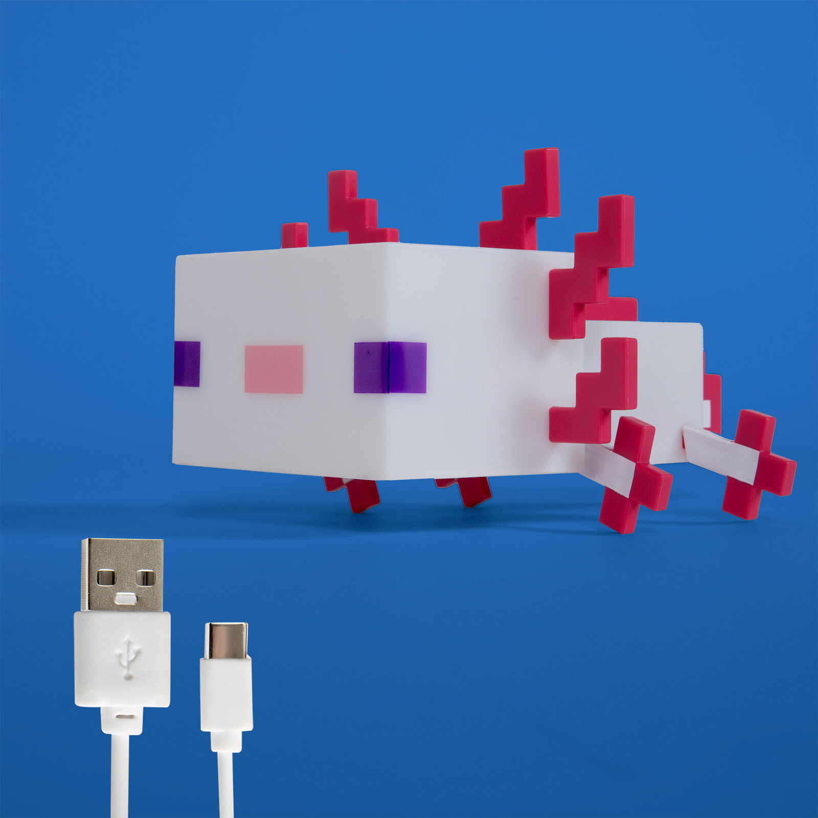 Weißes, pixelartiges Axolotl-LED-Nachtlicht mit pinken 3D-Kiemen und violetten Augen auf blauem Hintergrund, darunter USB-A- und USB-C-Ladekabel; Perspektive: frontale Seitenansicht leicht von oben.