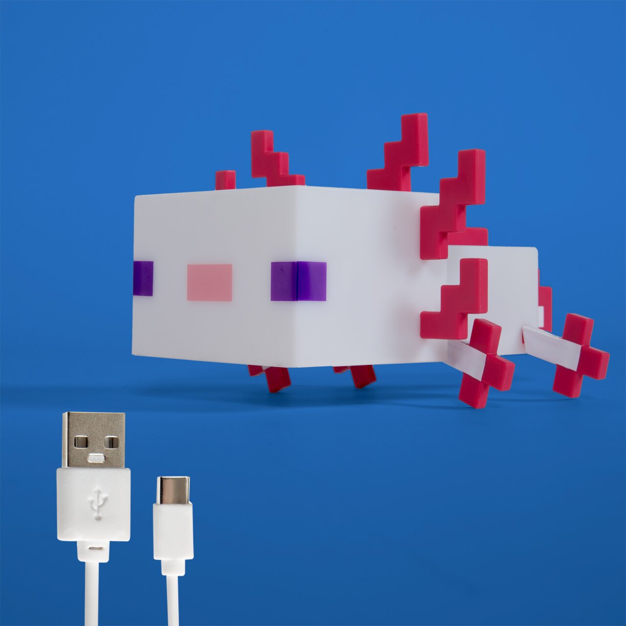 Wit, pixelachtig axolotl-led-nachtlampje met roze 3D-kieuwen en paarse ogen op een blauwe achtergrond, met daaronder USB-A- en USB-C-oplaadkabels; perspectief: vooraanzicht, licht van bovenaf.