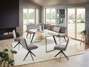 Moderne Esszimmer-Eckbankgruppe mit grauen Polstern und einem Holztisch, umgeben von großen Fenstern mit Blick auf den Garten. Perspektive von schräg vorne.