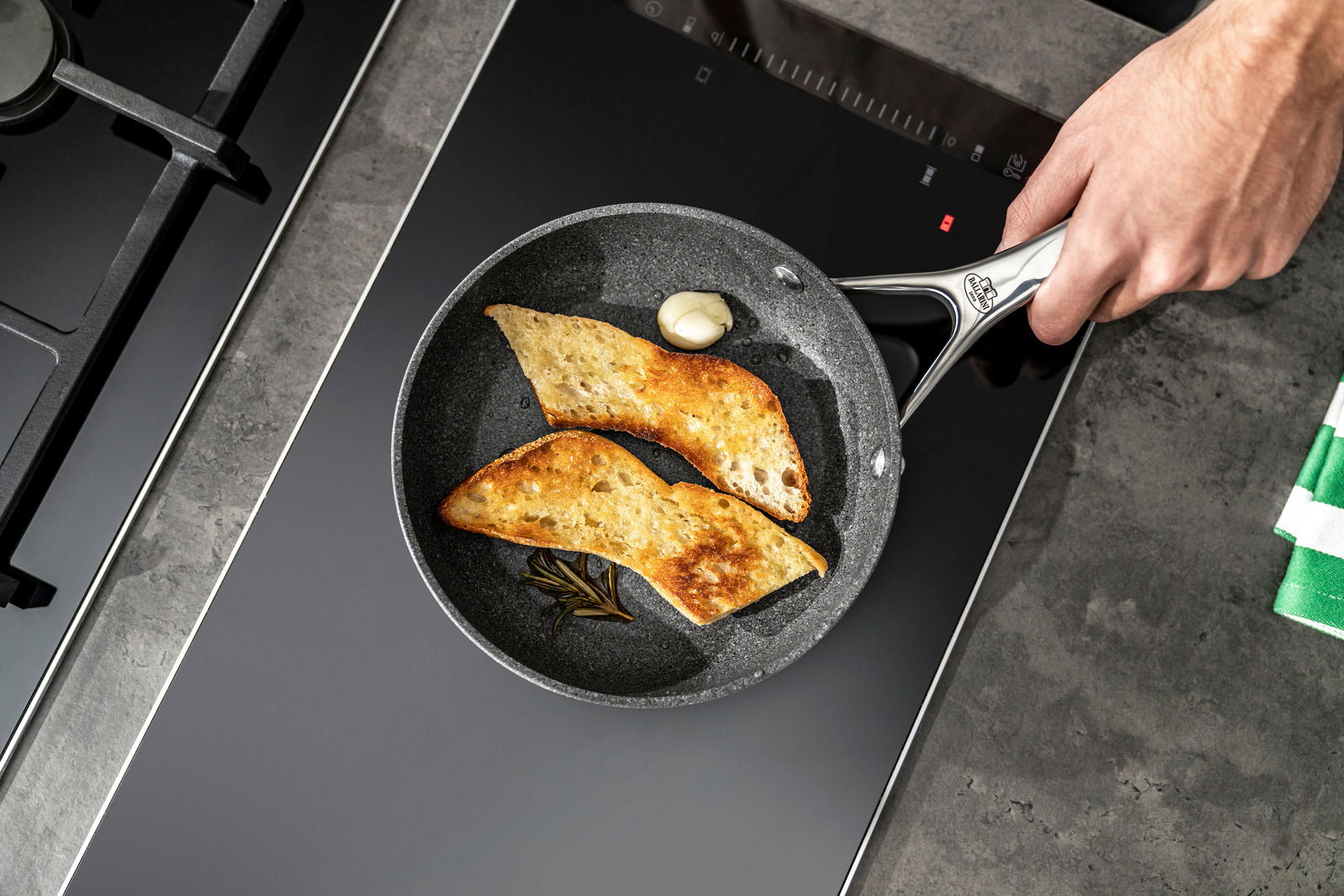 Bratpfanne mit 20 cm Durchmesser, von oben fotografiert, mit zwei Scheiben geröstetem Brot, Knoblauch und Rosmarin.