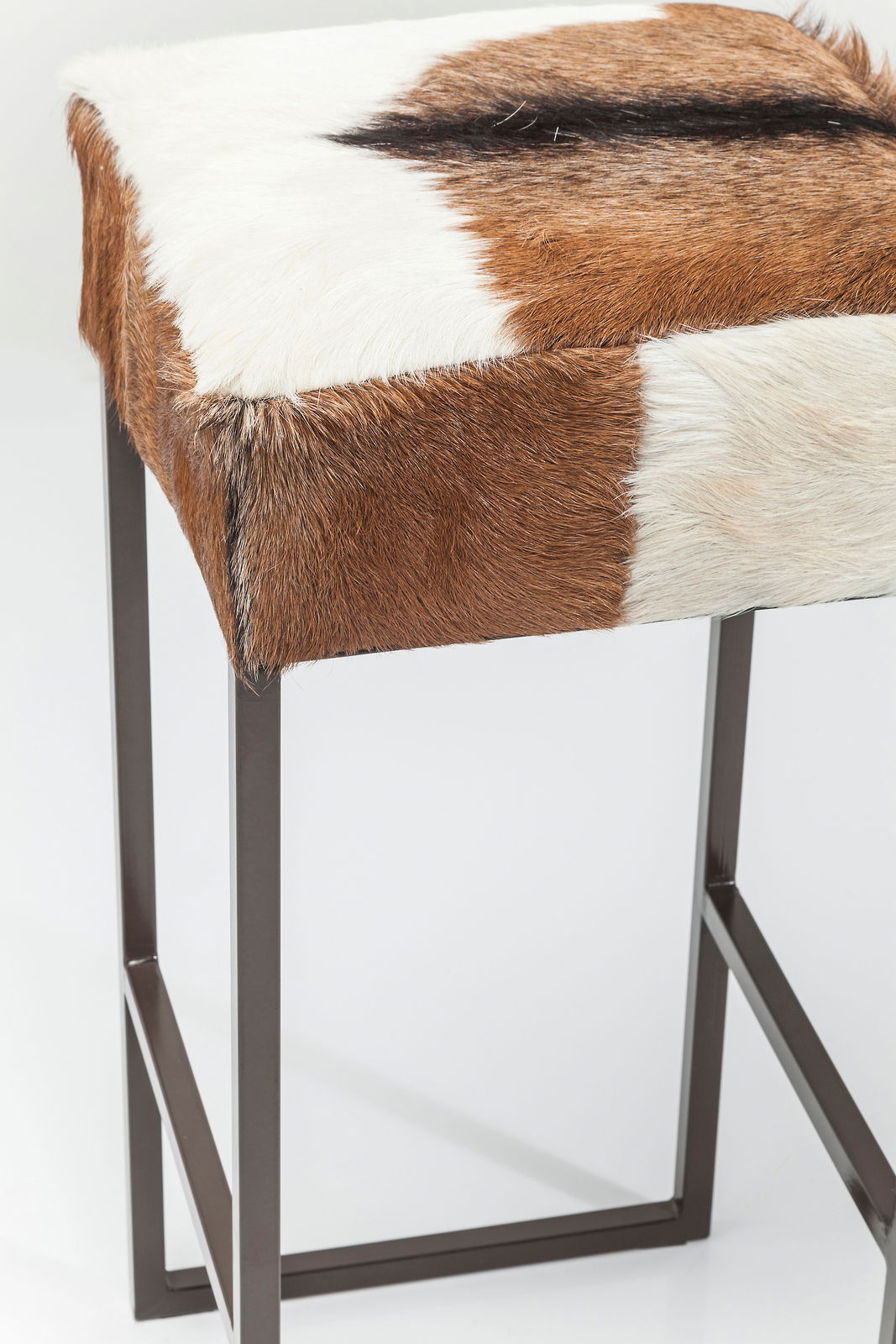 Hocker mit braun-weißer Felloberfläche und Metallgestell, seitliche Perspektive