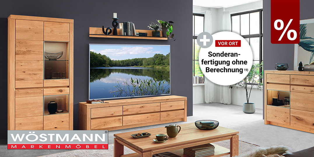 Modernes Wohnzimmer mit massiven Eichenmöbeln von Wöstmann, bestehend aus Vitrine, TV-Lowboard, Sideboard und Couchtisch vor dunkelgrauer Wandgestaltung.