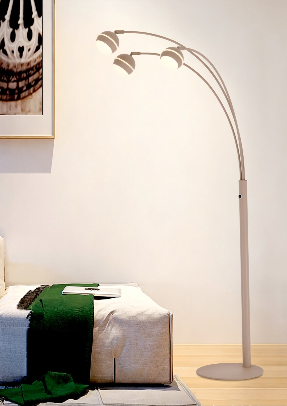 Moderne beige boogvloerlamp met drie verlichte, ronde lampenkappen naast een bank, gezien in volledig zijaanzicht.