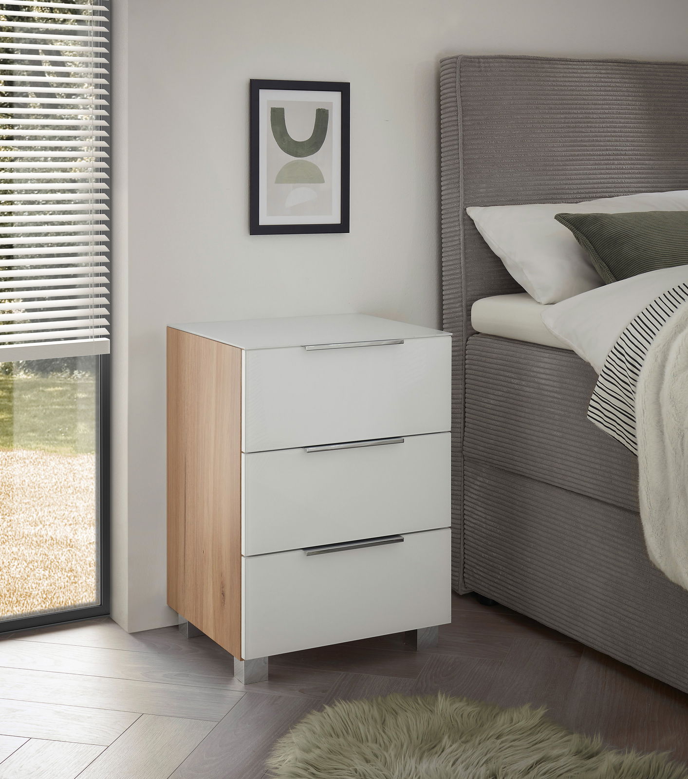 Moderne Nachtkommode mit drei Schubladen, weiß glänzend mit Holzseiten, seitliche Perspektive neben einem Bett.