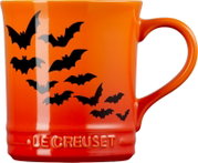 Orangefarbene Le Creuset Tasse mit schwarzen Fledermausmotiven und großem Henkel, frontal aus leichter Seitenperspektive
