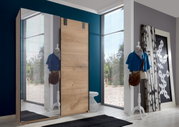 Schwebetürenschrank mit Holz- und Spiegelfront, seitliche Perspektive, im modernen Raum mit Schaufensterpuppe und Kunstwerk.