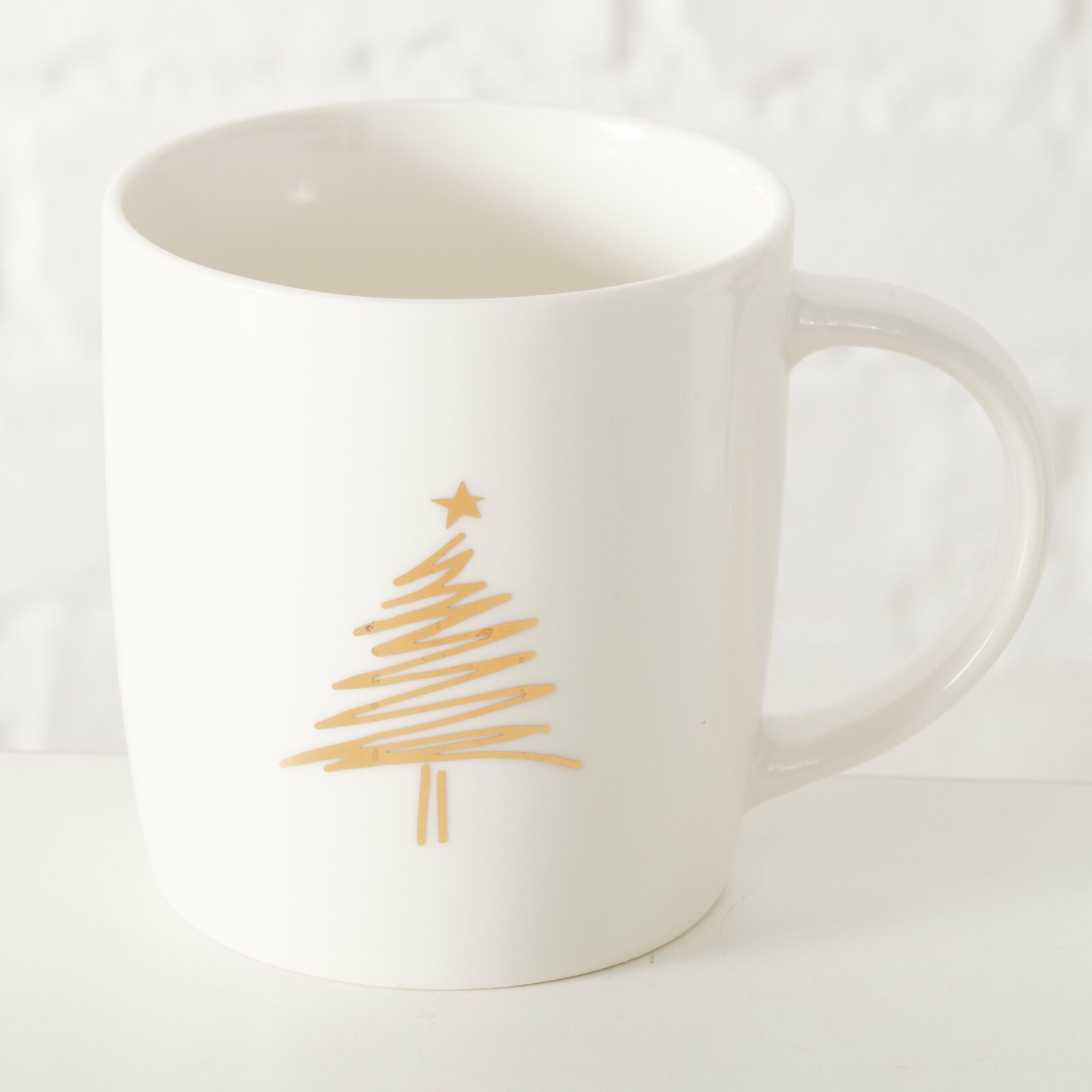 Weißer Becher mit goldener Weihnachtsbaum-Grafik, seitliche Perspektive