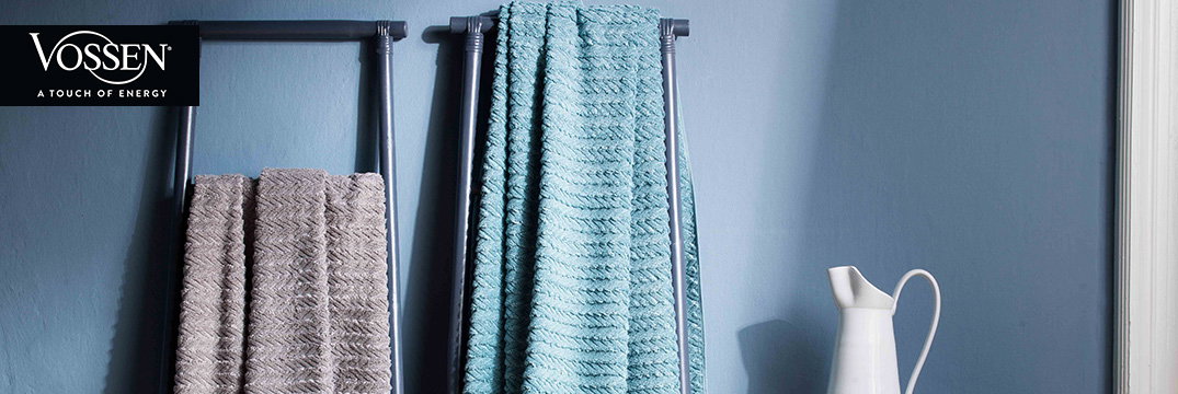Zwei weiche Handtücher in Grau und Blau hängen auf schwarzen Haltern vor einer blauen Wand im Badezimmer.