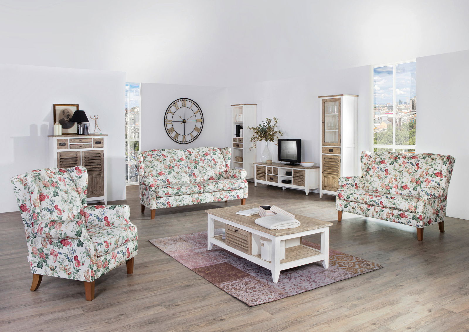 Zurbrüggen Sofabank 2,5-sitzig KIMBERLY Wohnzimmer mit floraler Sofagarnitur, bestehend aus einem 2,5-sitzigen Sofa und einem Sessel, in einer hellen, modernen Umgebung. Perspektive: Frontalansicht auf die Sofagarnitur.