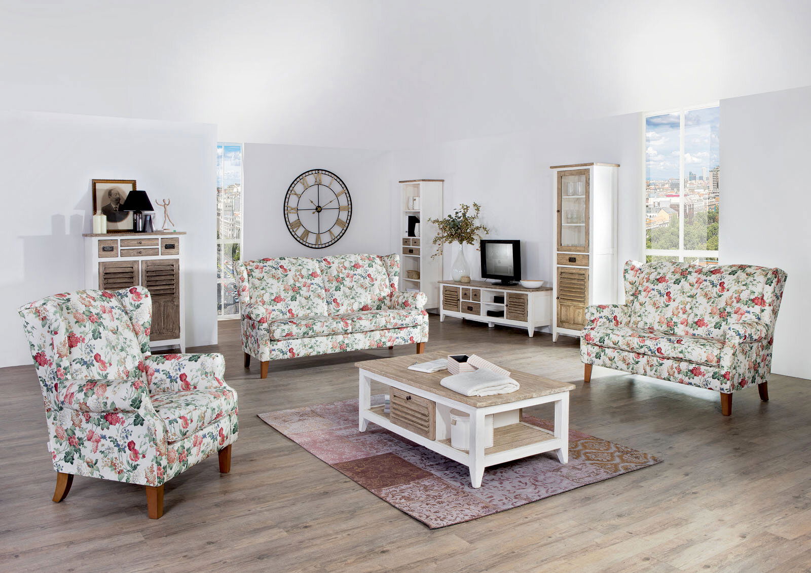 Wohnzimmer mit floraler Sofagarnitur, bestehend aus einem 2,5-sitzigen Sofa und einem Sessel, in einer hellen, modernen Umgebung. Perspektive: Frontalansicht auf die Sofagarnitur.