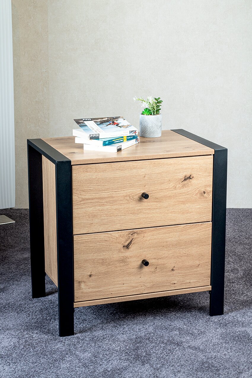 Moderne Kommode mit zwei Schubladen in Eichenholz-Optik und schwarzem Rahmen, frontal leicht von oben fotografiert; oben liegen Bücher und ein kleiner Blumentopf.
