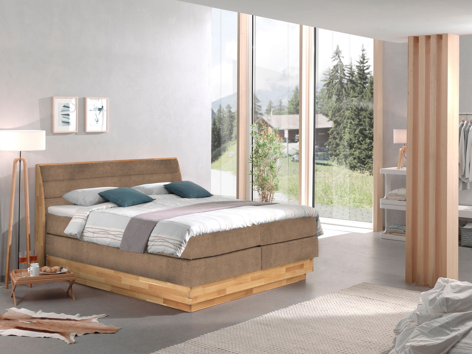 Modernes Boxspringbett in einem hellen, stilvollen Schlafzimmer mit großen Fenstern und Blick auf die Natur, seitliche Perspektive.