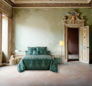 Elegante grüne Bettwäsche in einem antiken Raum mit kunstvoller Wandverzierung, frontal betrachtet.
